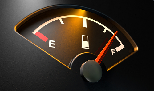 A closeup of a backlit illuminated gas gage with the needle indicating a near full tank on an isolated dark background